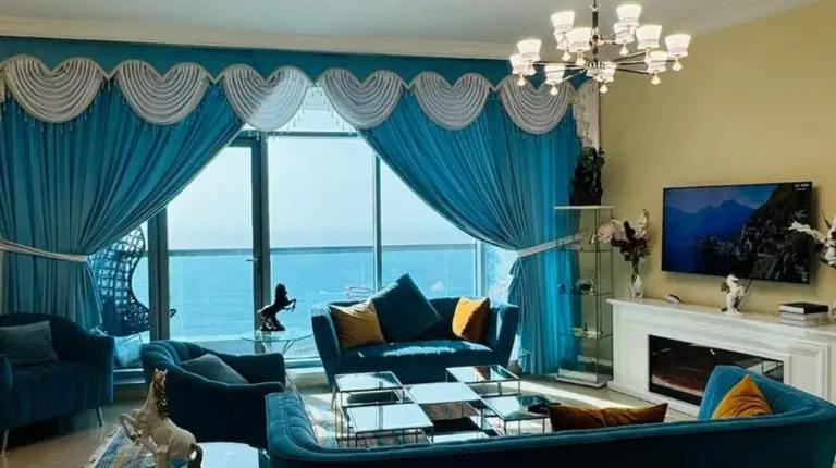 una sala de estar con gran sofá azul y cortinas azules en Ajman Luxurious Holiday Homes en Ajman
