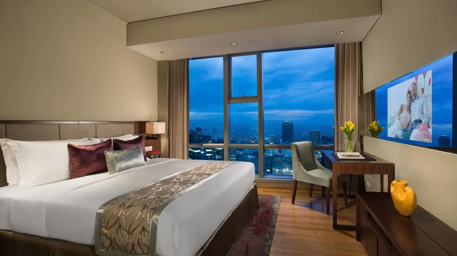 ein Schlafzimmer mit einem Bett, einem Schreibtisch und einem groÃen Fenster im Ascott Kuningan Jakarta in Jakarta