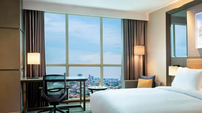 a hotel room with a bed and a desk and a large window at DoubleTree by Hilton Surabaya in Surabaya