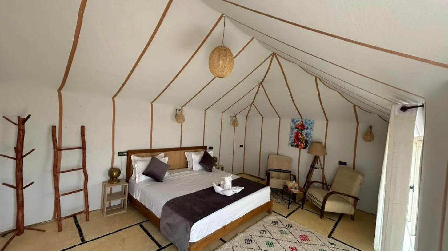 une chambre avec un lit Ã  baldaquin et une chaise au Golden Dunes Luxury Camp Ã  Merzouga