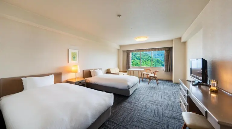 una habitaciÃ³n de hotel con dos camas y un televisor en Grand Mercure Beppu Bay Resort & Spa en Beppu