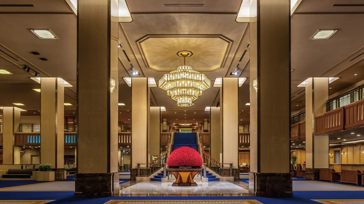 eine Lobby mit einem Kronleuchter und einer Treppe in einem GebÃ¤ude im Imperial Hotel Tokyo in Tokio
