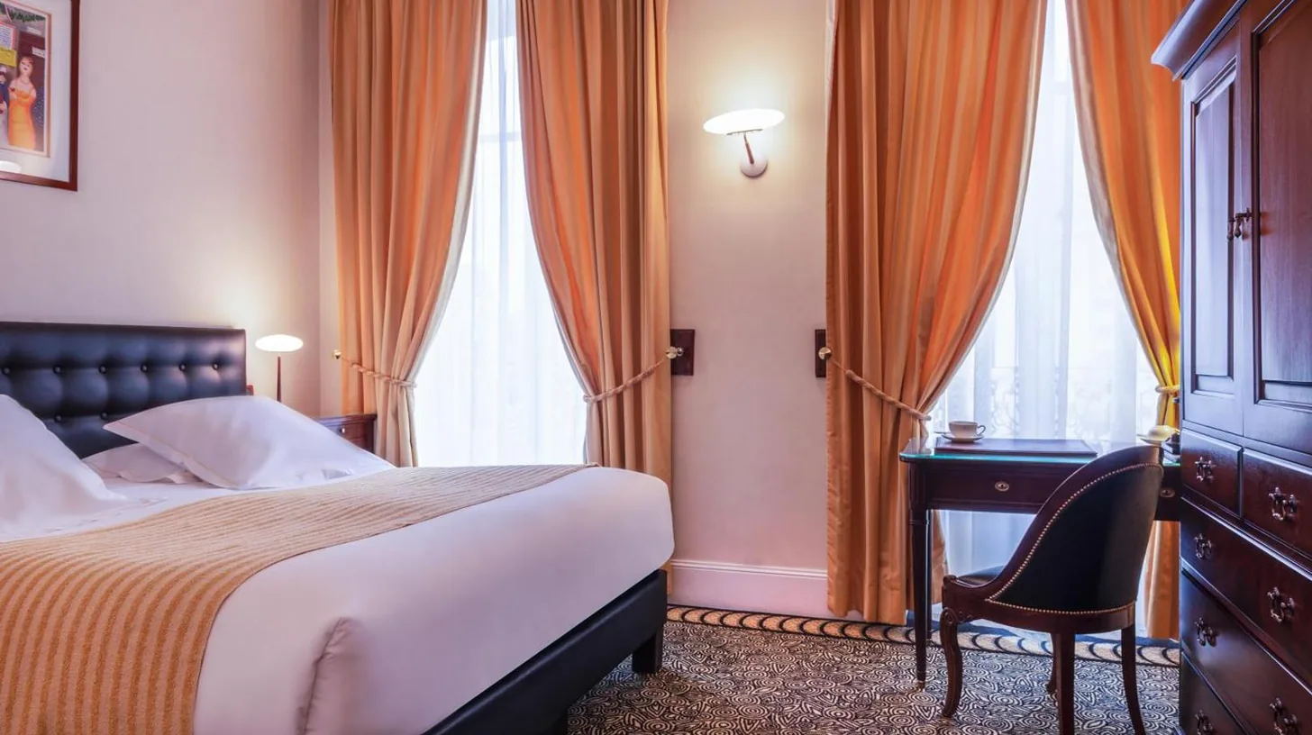 a bedroom with a bed and a desk and windows at L'Hôtel in Beaune
