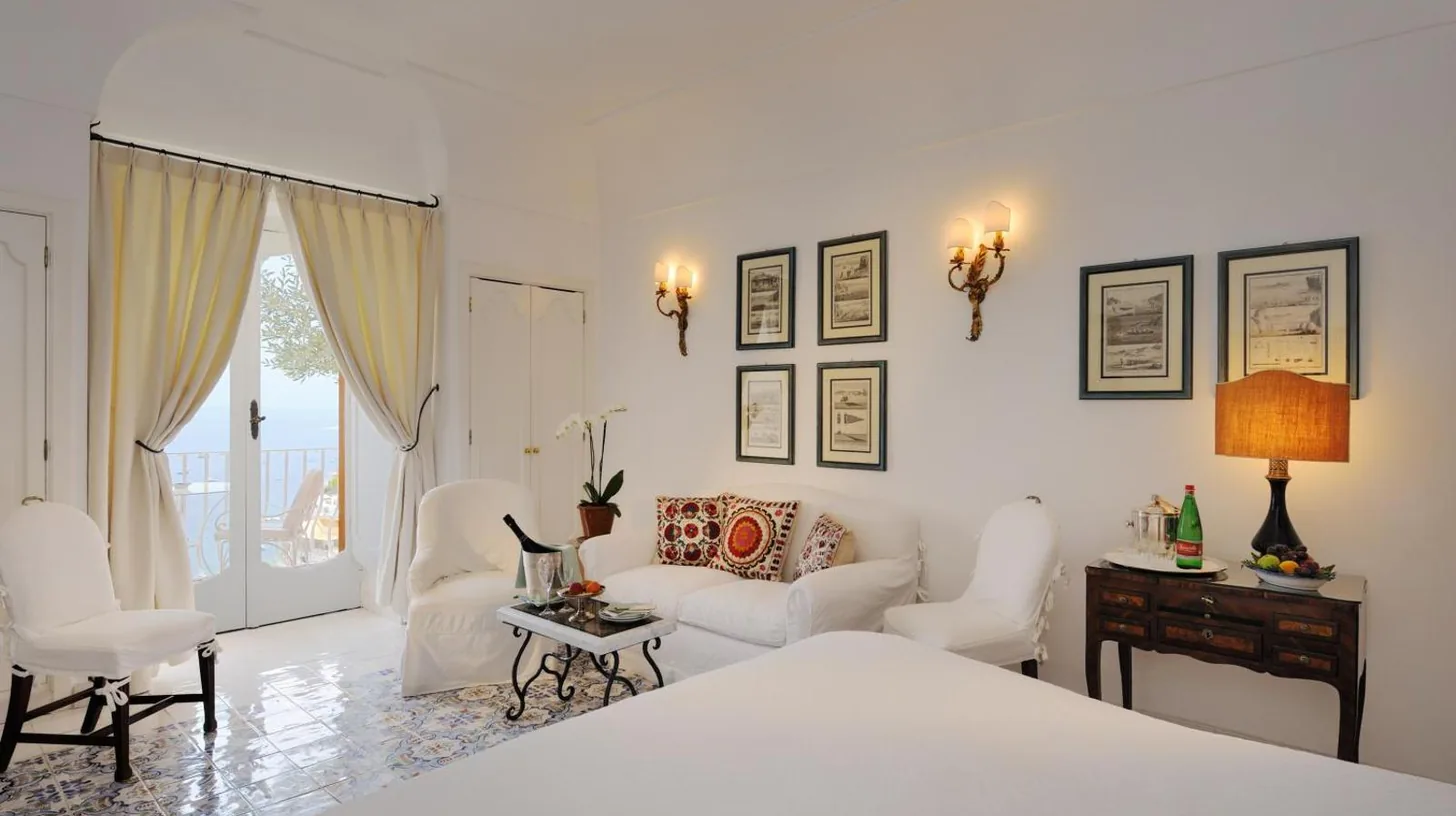 a white bedroom with a bed and a living room at Le Sirenuse in Positano