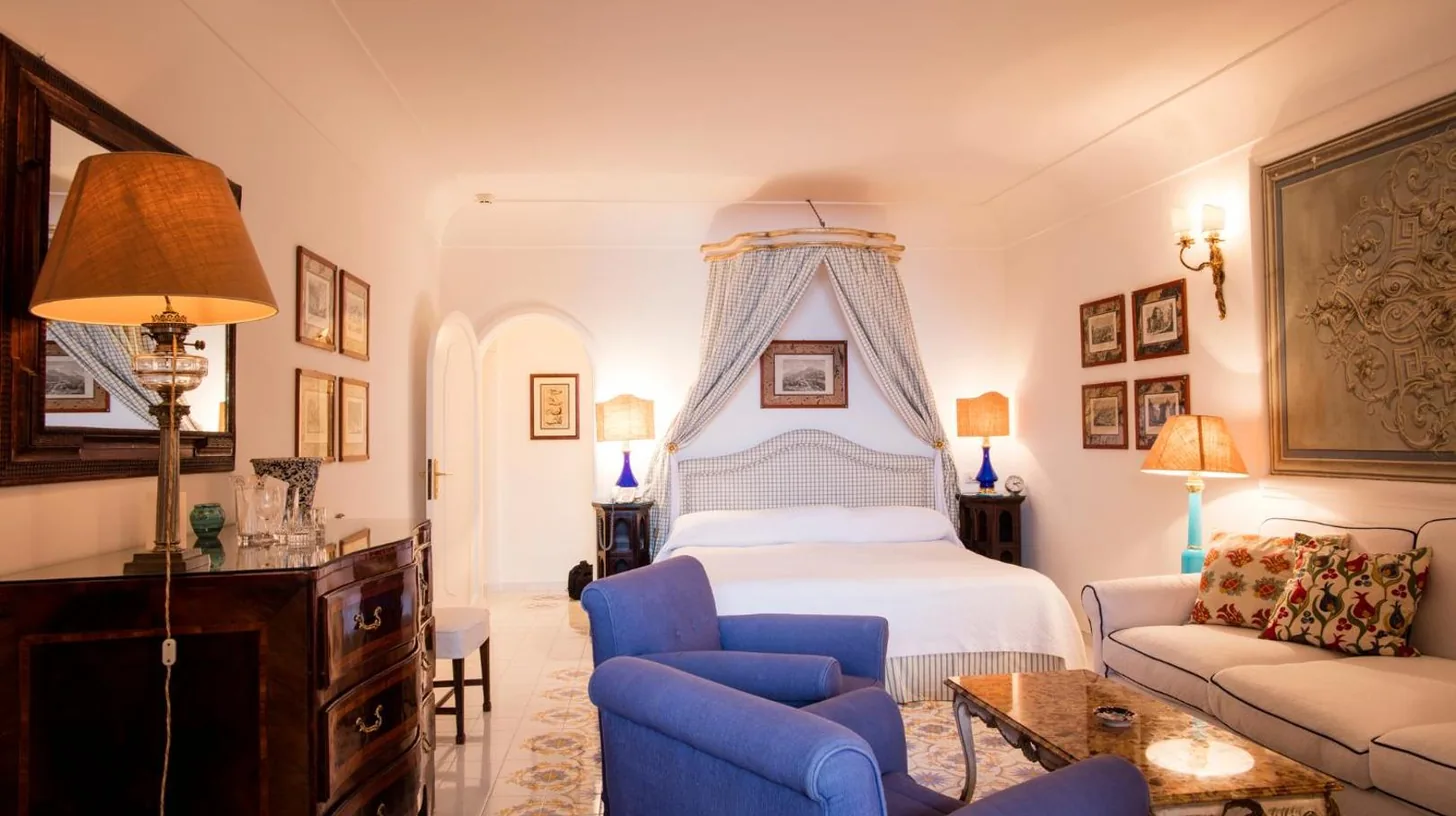 a bedroom with a bed and a blue chair and a couch at Le Sirenuse in Positano