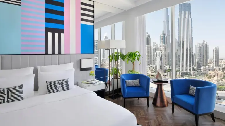 un dormitorio con una cama blanca y una silla azul en Pullman Dubai Downtown en DubÃ¡i