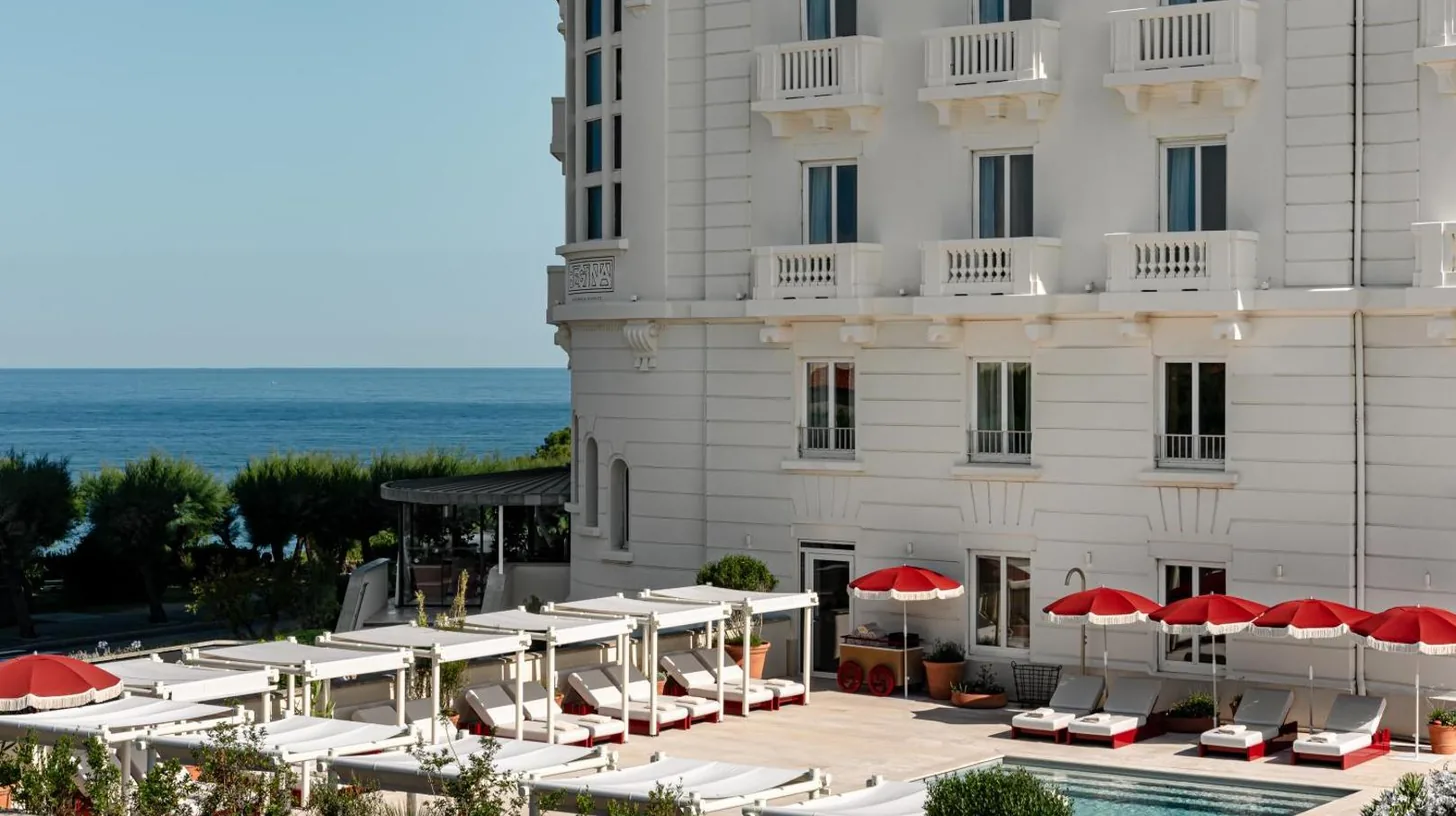 a hotel with a pool and chairs and umbrellas at Regina Experimental Biarritz in Biarritz