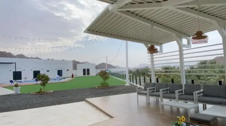 a patio with chairs and tables and a large white pergola at Sheema Lodge in Hatta