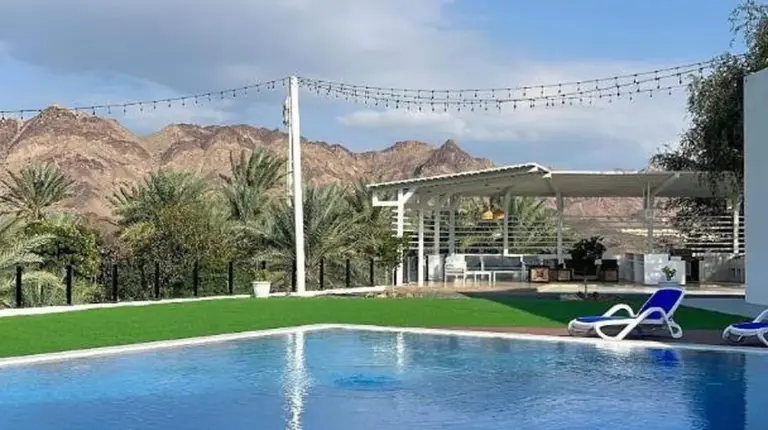 a large swimming pool with blue water and mountains in the background at Sheema Lodge in Hatta
