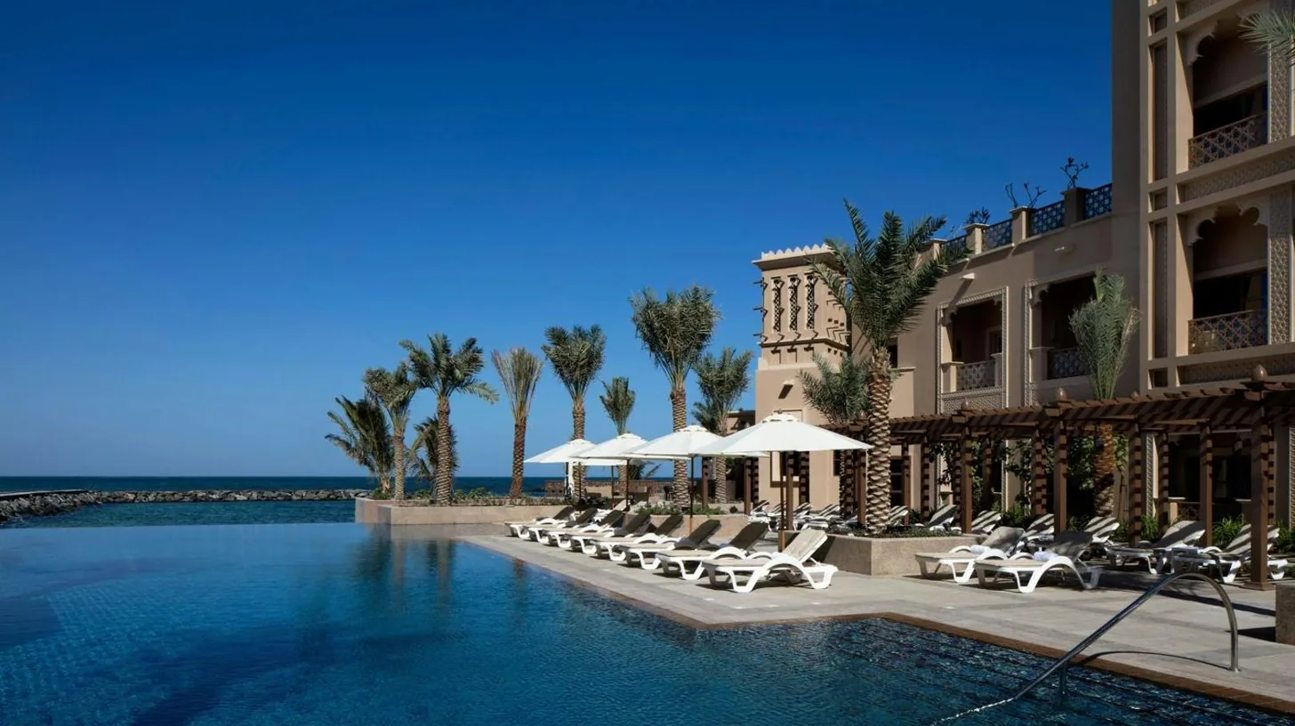 a swimming pool with lounge chairs and a building at Sheraton Sharjah Beach Resort and Spa in Sharjah