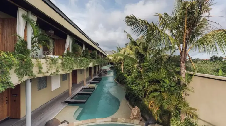 un pasillo de hotel con piscina y palmeras en Sini Vie Resort & Spa Seminyak by Ini Vie Hospitality en Seminyak