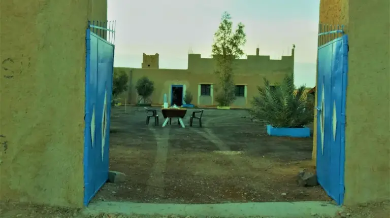 a courtyard with blue doors and a picnic table at Tifinagh Guest House in Merzouga
