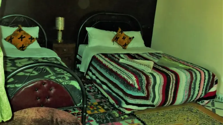 a bedroom with two beds and a chair and a rug at Tifinagh Guest House in Merzouga