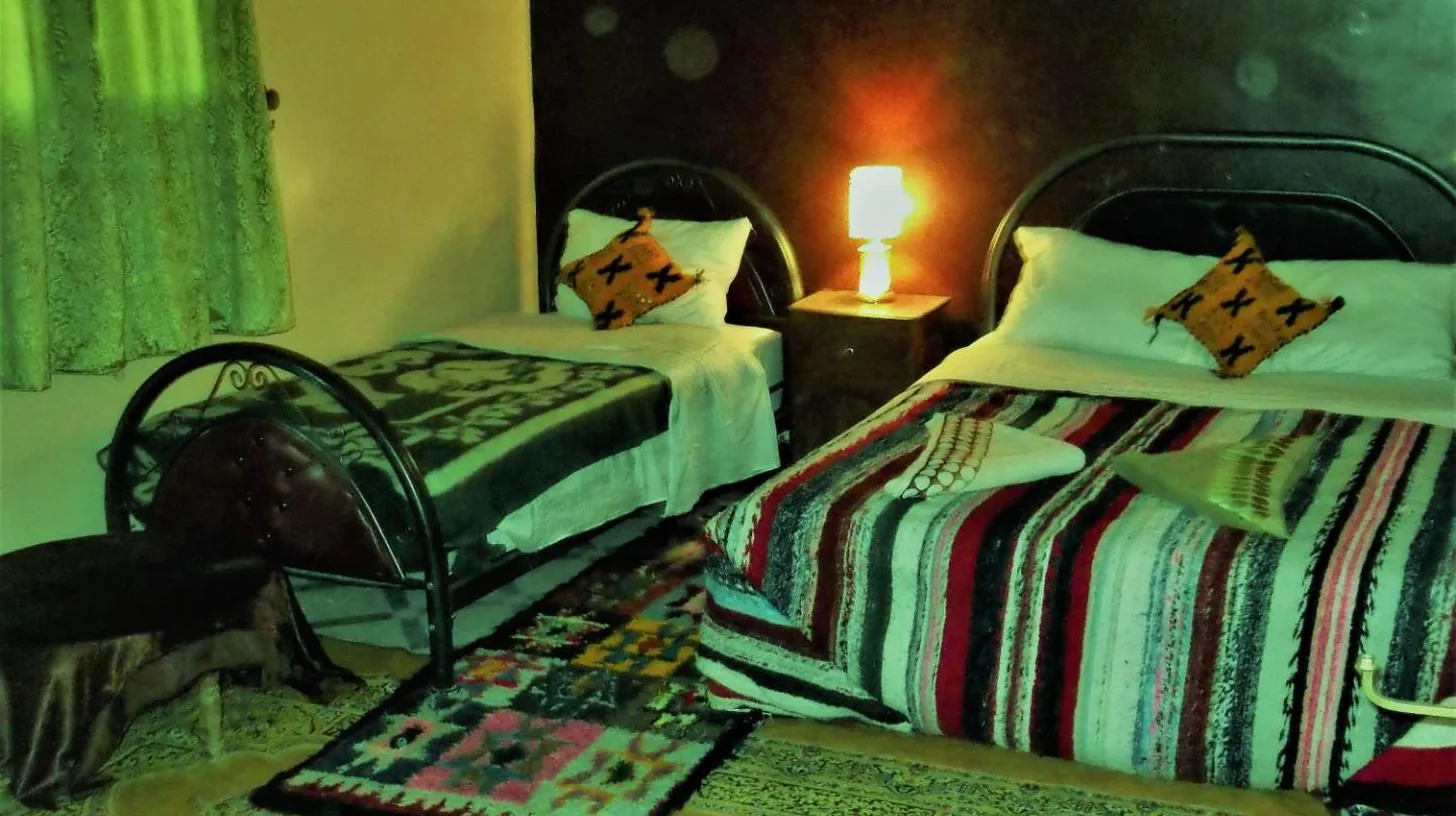 a bedroom with two beds and a table with a lamp at Tifinagh Guest House in Merzouga