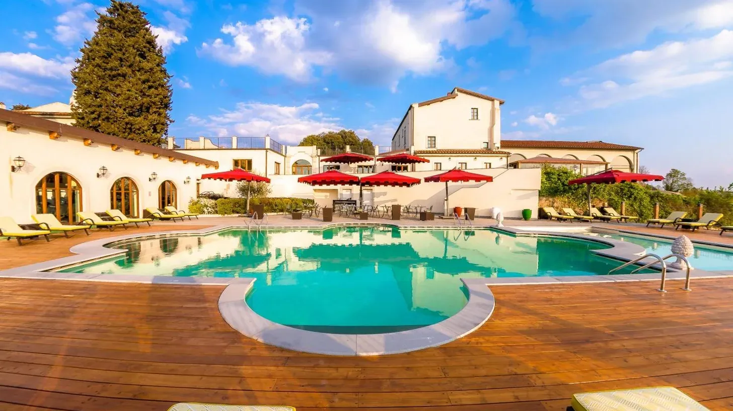 ein Schwimmbad in einem Resort mit roten Sonnenschirmen im Villa Tolomei Hotel & Resort in Florenz